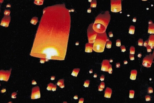 A group of people flying paper lanterns in the dark.