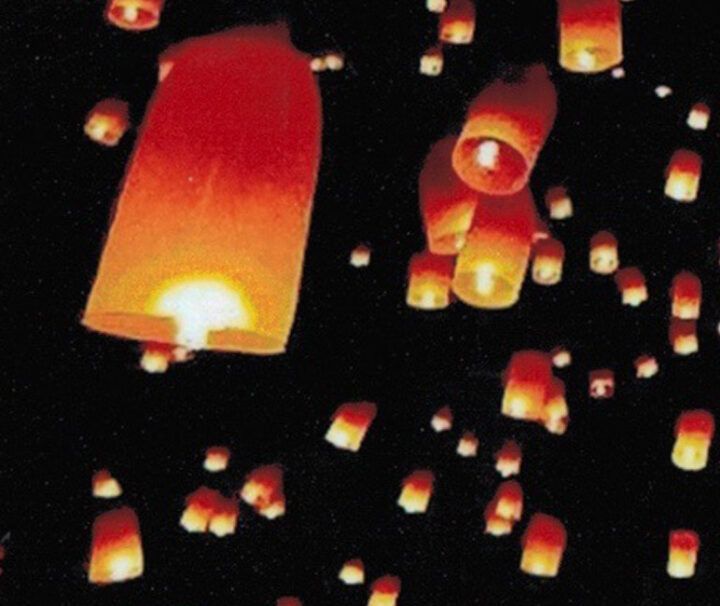 A group of people flying paper lanterns in the dark.